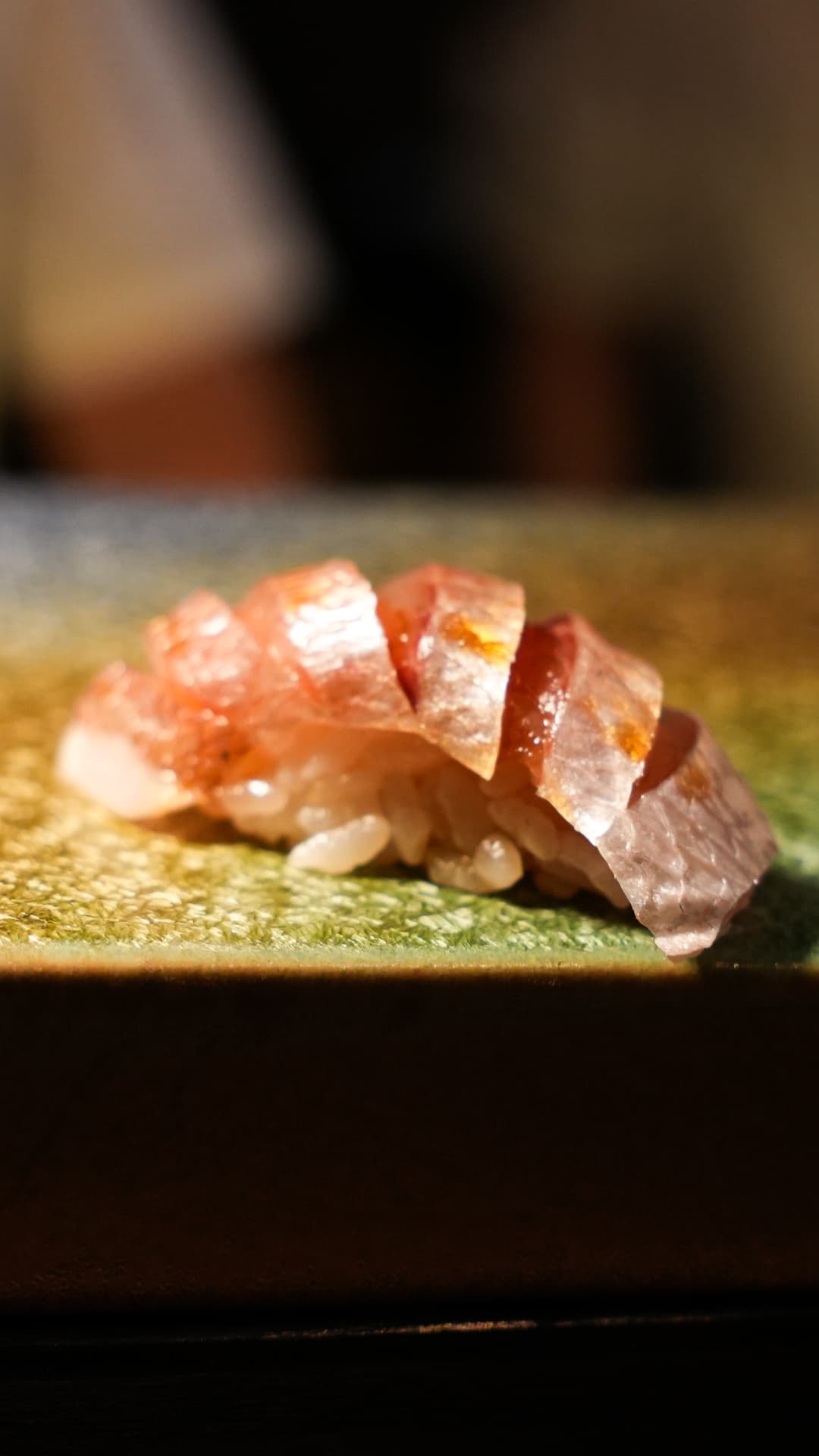 Glistening slice of fish over seasoned rice on a green ceramic plate