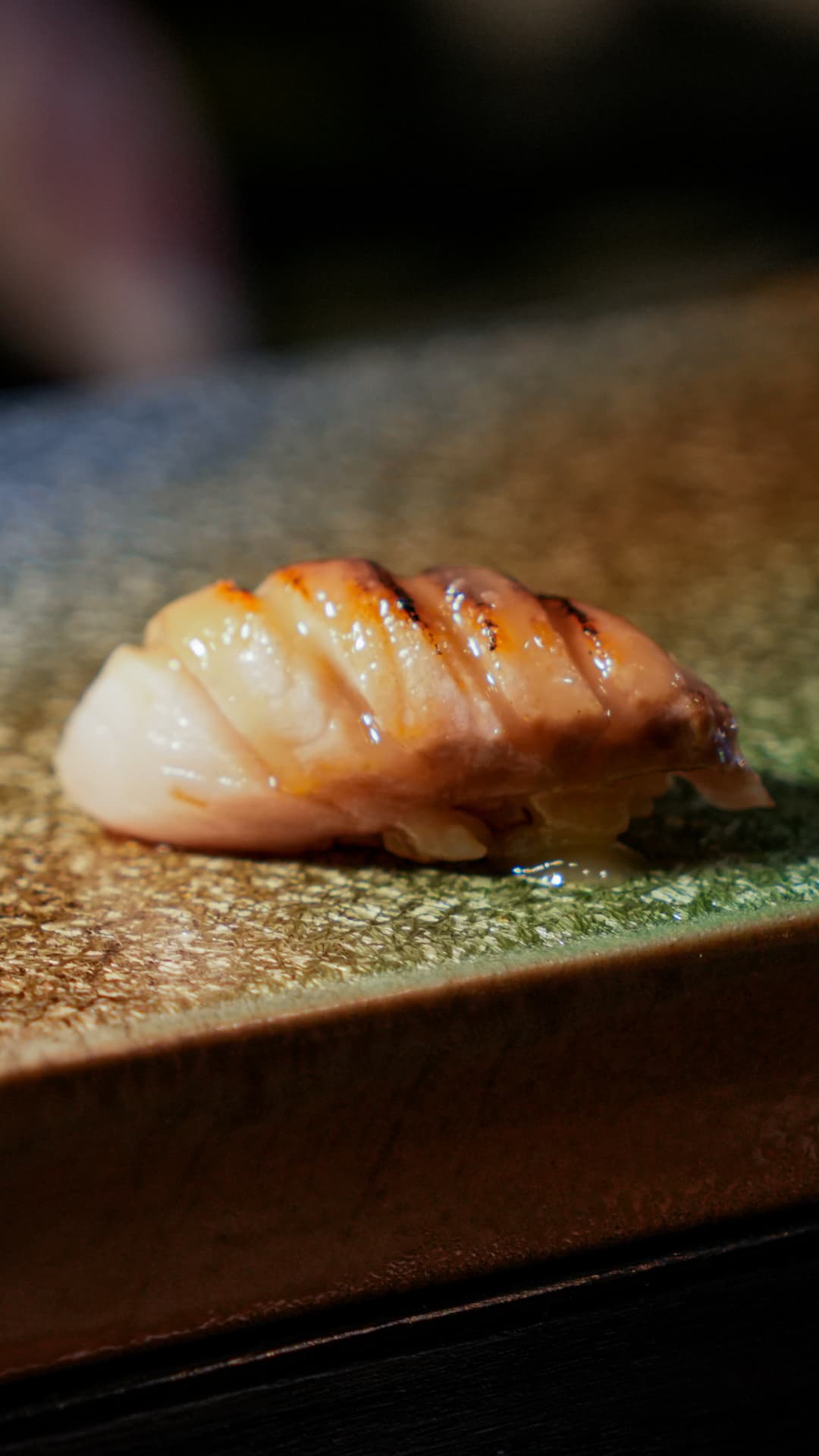 Grilled scallop nigiri with charred edges on a green ceramic plate