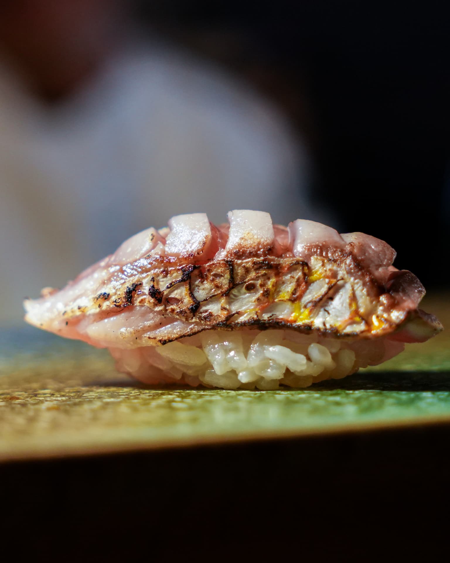 Lightly torched nigiri with crisped skin resting on warm rice