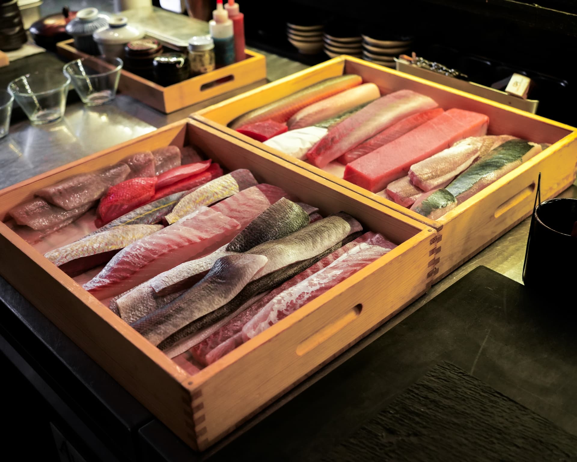 Two wooden neta boxes filled with the day's fish behind the sushi counter
